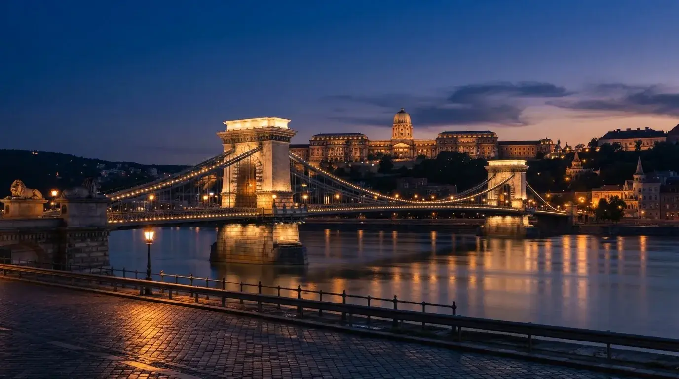 A budapesti Lánchíd esti fényekben a Duna fölött, a háttérben a budai Vár, forgalom nélküli rakpart.